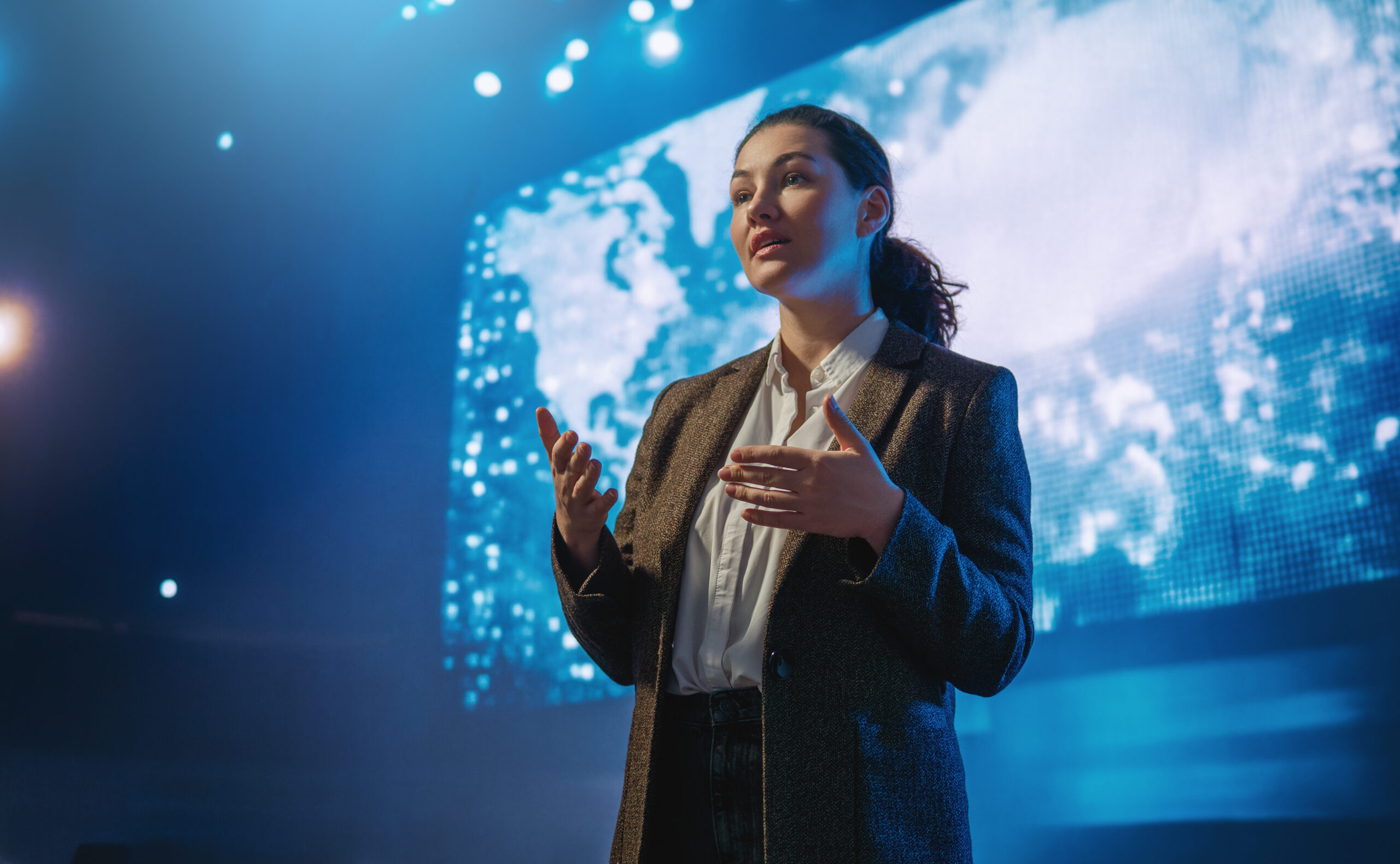 Female executive delivering a keynote presentation on global strategy and leadership visibility with digital world map background