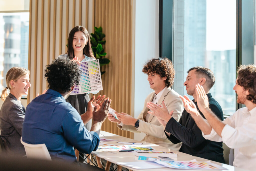 Employees applauding a colleague during a team meeting in a modern office, highlighting employee engagement, workplace culture, and leadership recognition.