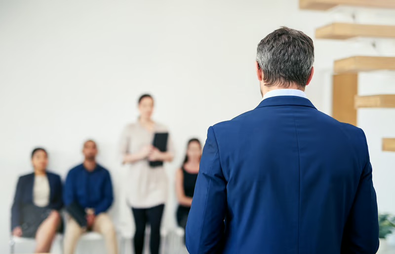 Business leader speaking with employees during a workplace meeting about company culture and communication.