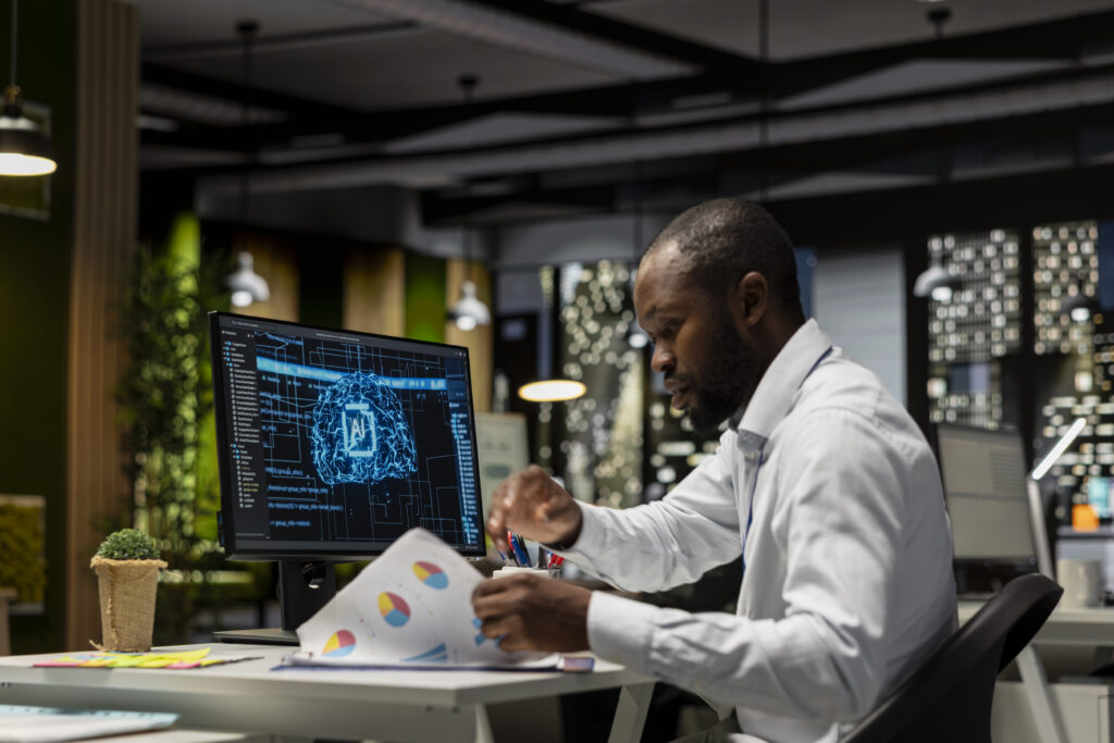 Business professional reviewing printed reports beside a computer displaying an artificial intelligence interface in a modern office.